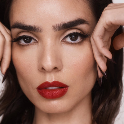 Semi-sheer, glossy 212 red lipstick on a model with olive skin undertones. Moisturizing, nourishing, hydrating, antioxidant-rich, and botanical-infused formula.