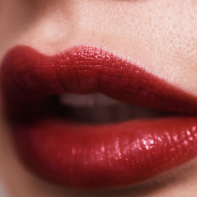 Semi-sheer, glossy 212 red lipstick on a model with olive skin undertones. Moisturizing, nourishing, hydrating, antioxidant-rich, and botanical-infused formula.