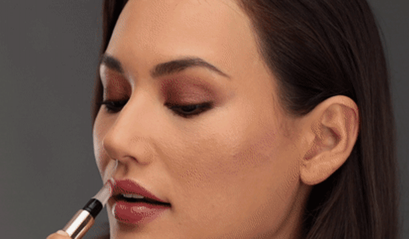 GIF of brown-haired light skin model in pink eyeshadow getting red lipstick removed by an off-camera makeup artist.