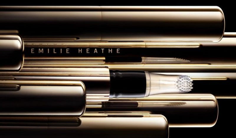 Emilie Heathe Exfoliating Lip R&R products stacked and repeated on top of and in front of each other. Packaging is thin, gold, cylindrical, and reflective. Product reads “EMILIE HEATHE.” Application tip is clear with small round bump-like bristles
