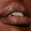 Mude mauve-nude lipstick on model with dark skin tone. Moisturizing, nourishing, hydrating, antioxidant-rich, and botanical-infused formula.